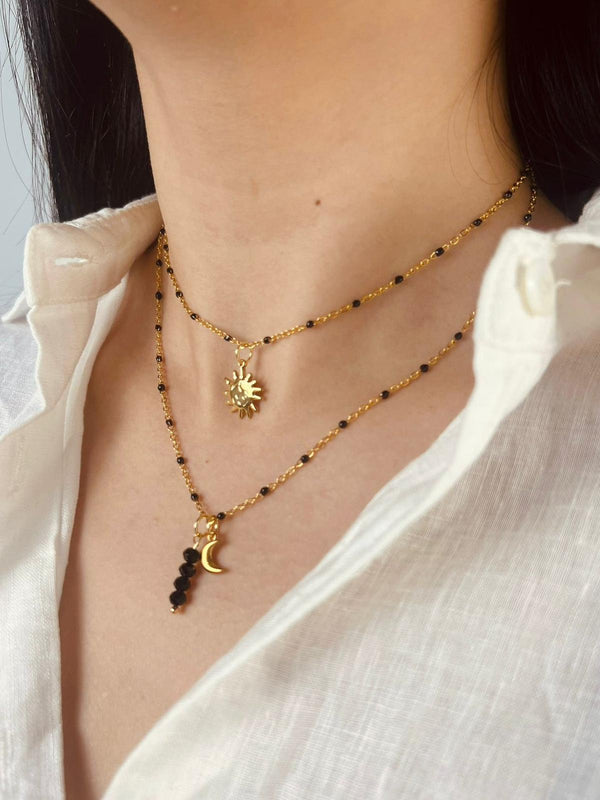 Necklace with sun and moon pendants on a person wearing a white shirt.