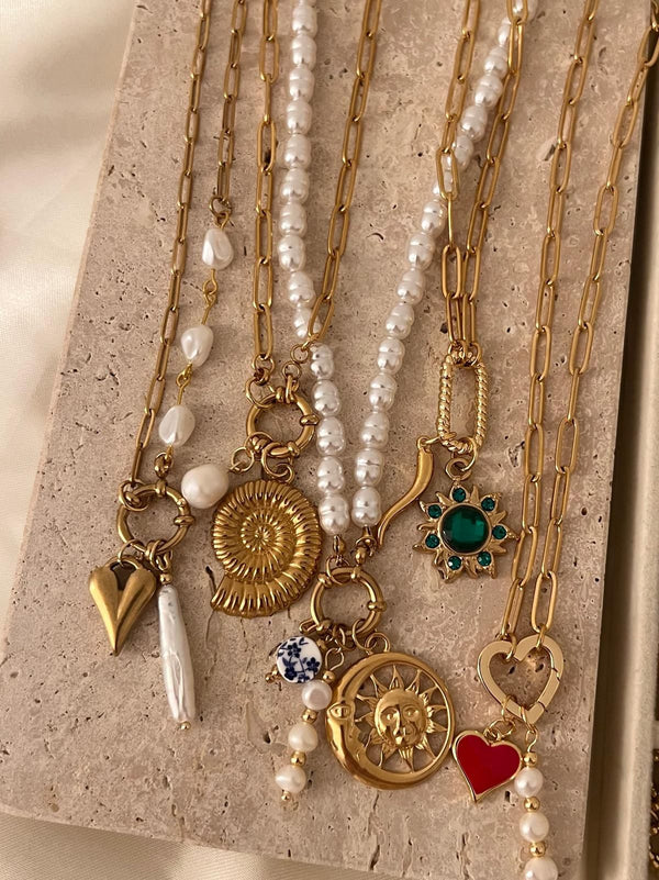 Set of gold and pearl necklaces with various charms on a textured surface