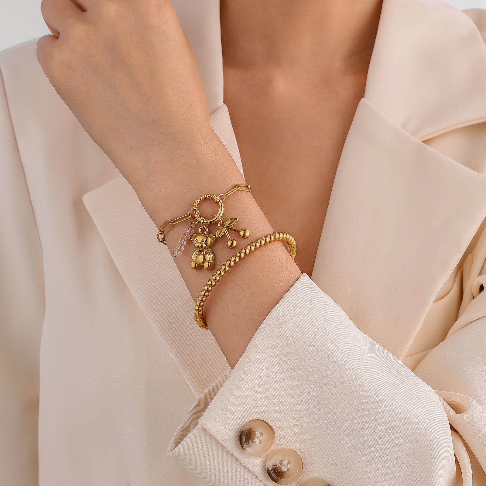 Gold bracelet with charms on a person wearing a beige suit.