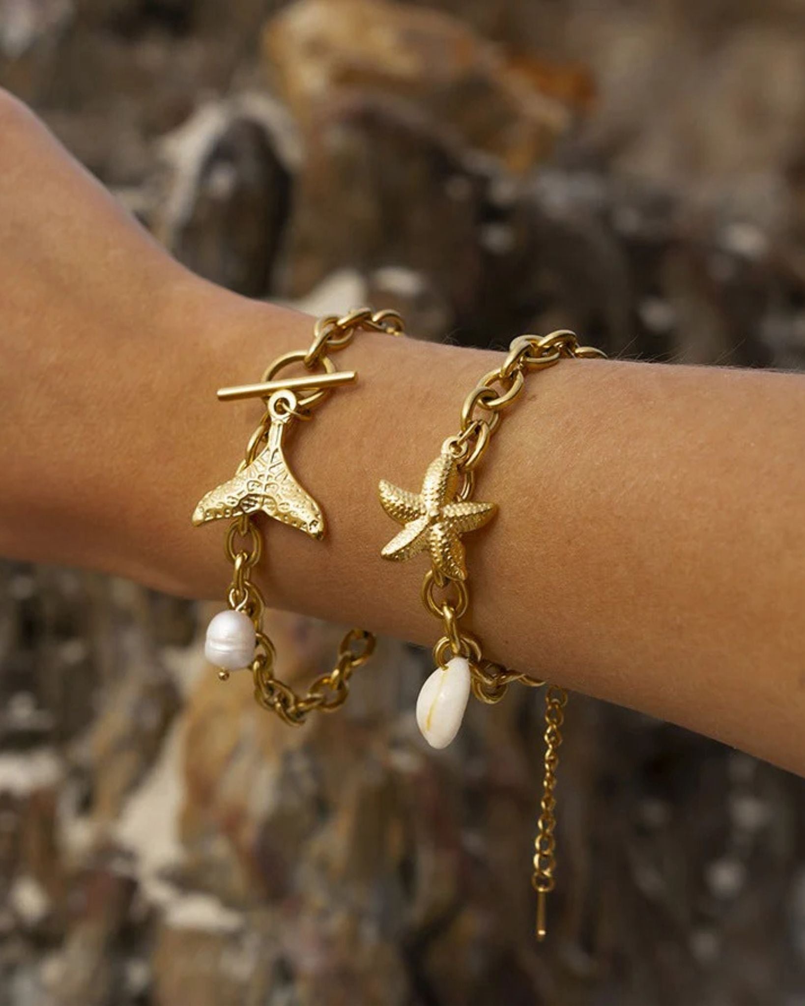 Gold bracelet with mermaid tail and starfish charm on a blurred natural background