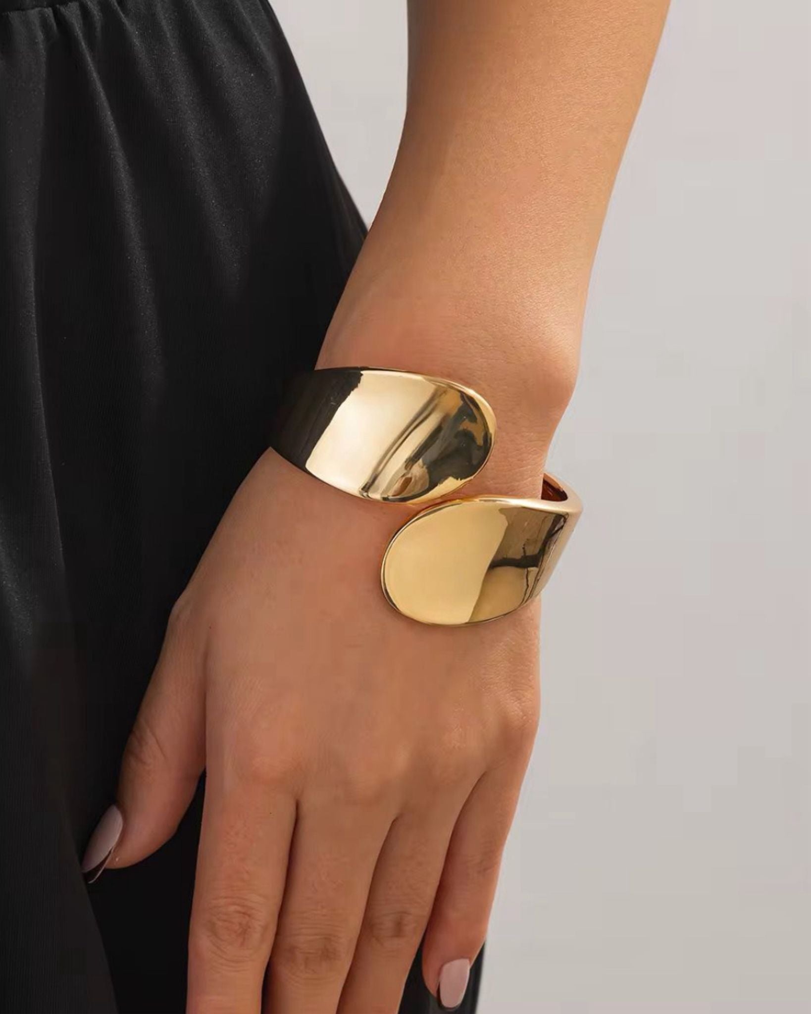 Gold ignis bangle on a wrist with a plain background