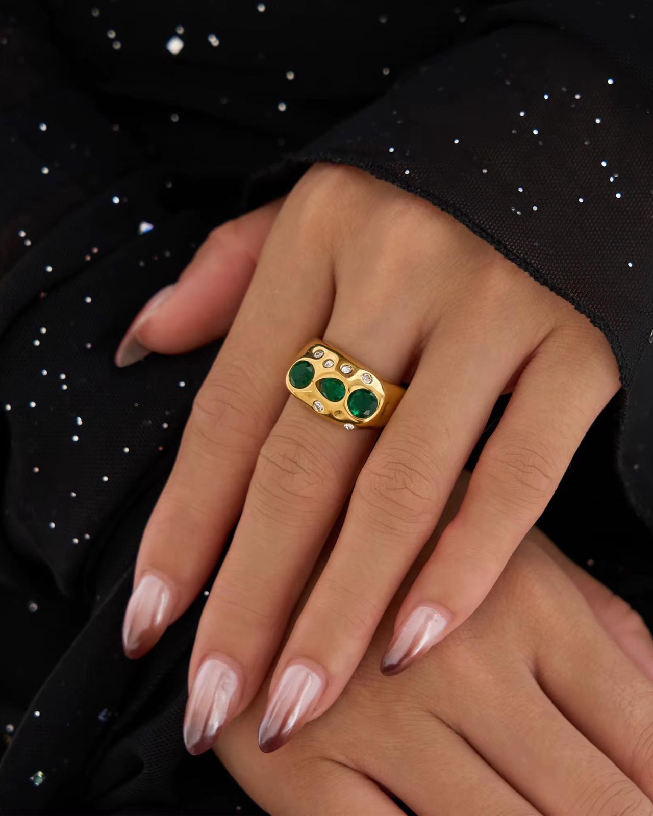 Gold scarlet ring with green gemstones on a hand against a black background