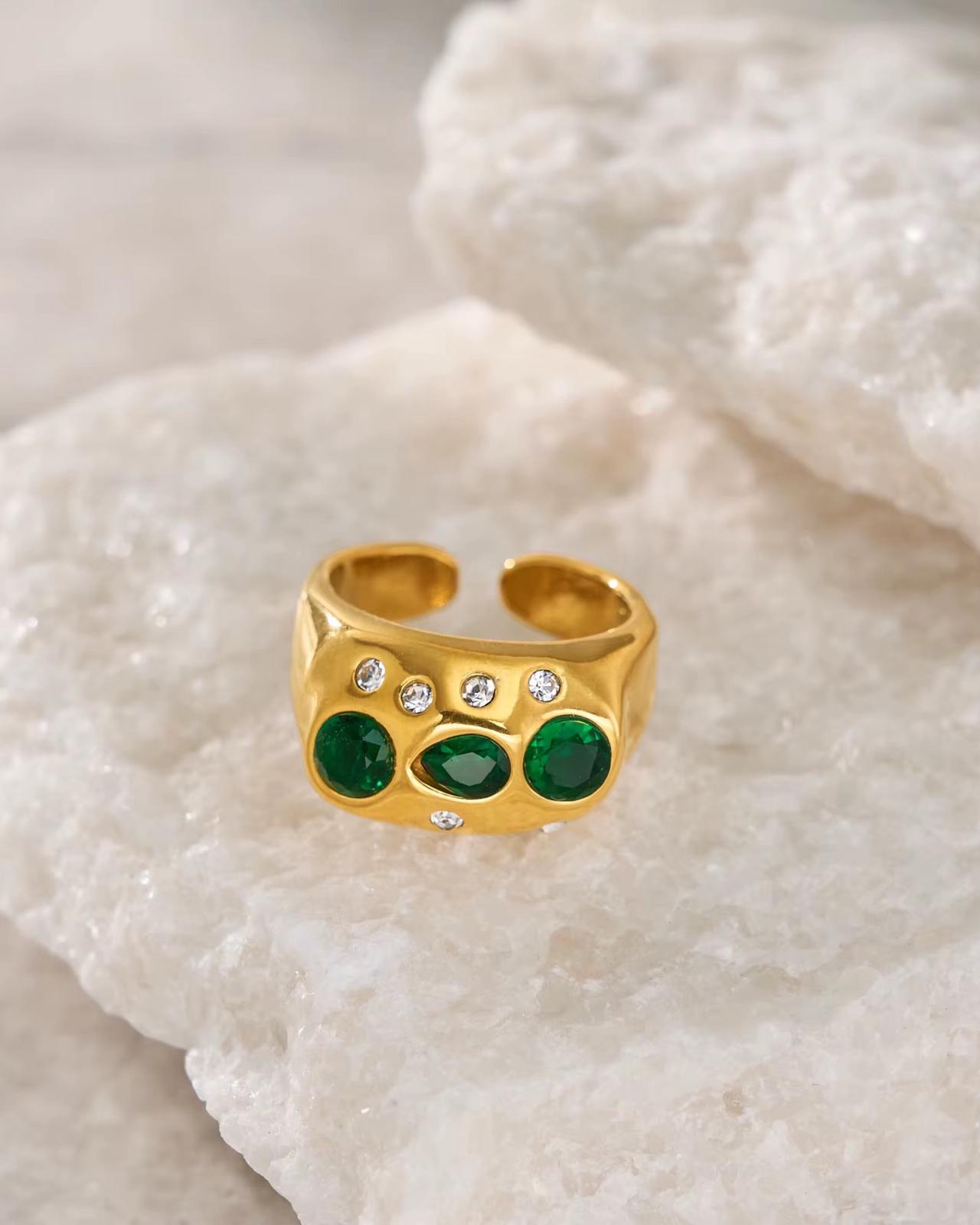Gold ring with green gemstones on a textured white surface