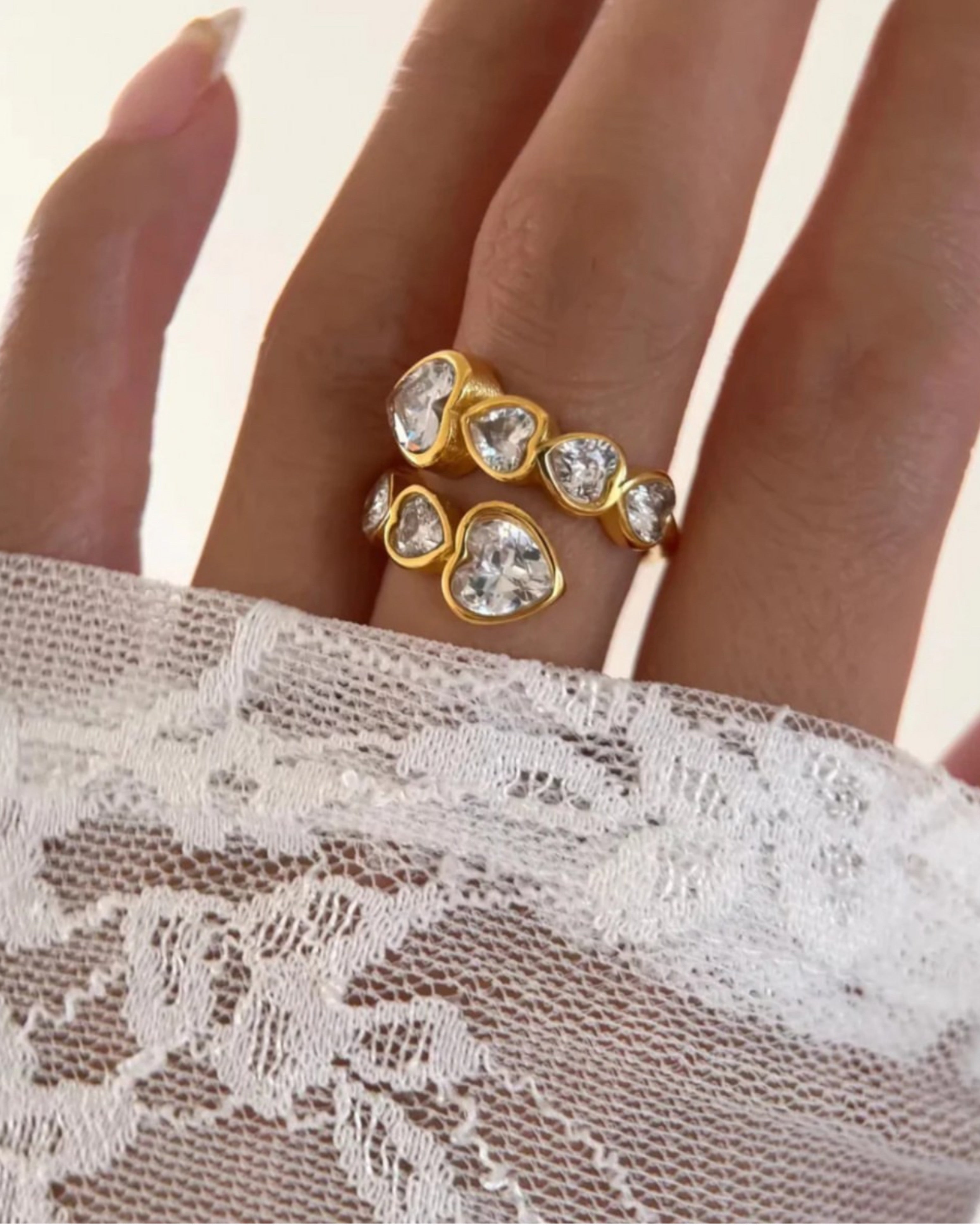 Gold zara heart ring with heart-shaped gemstones on a lace fabric background