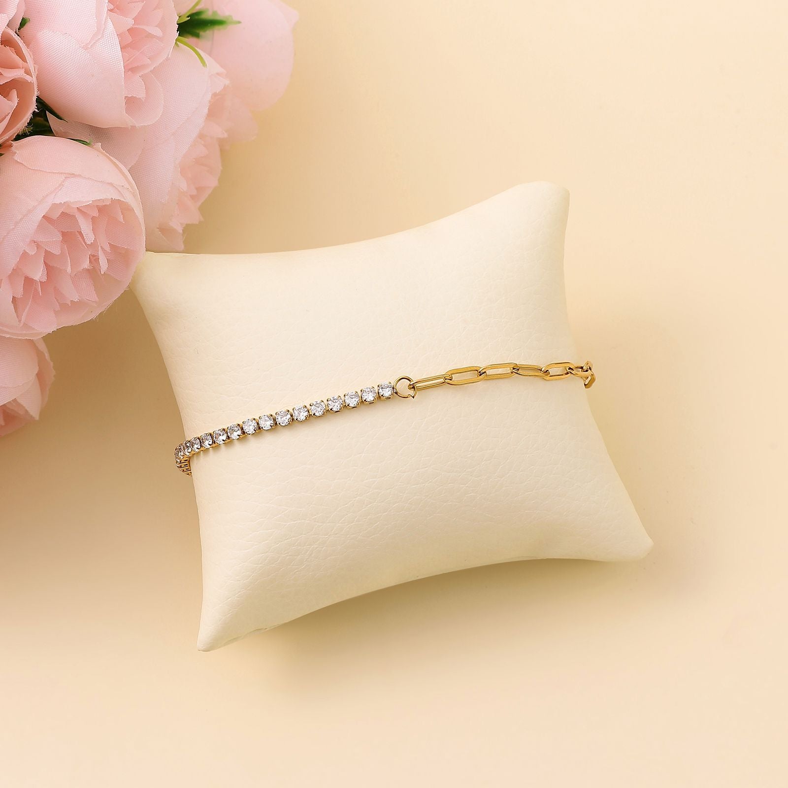 Gold zircon paper clip bracelet with crystals on a beige pillow with pink flowers in the background