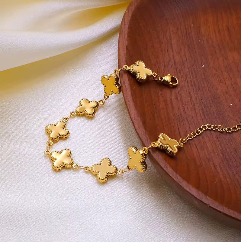 Gold louise clover bracelet with clover-shaped charms on a wooden plate.