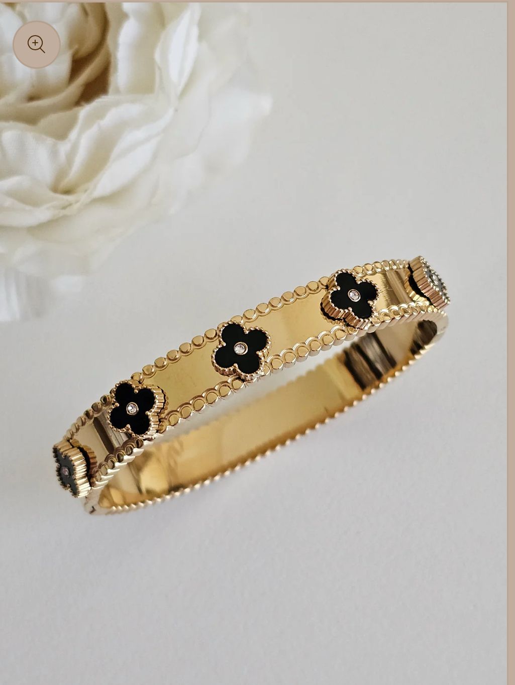An 18k gold plated stainless steel helen bangle bracelet with a black and gold pattern, featuring zirconia clover accents, displayed on a white surface.