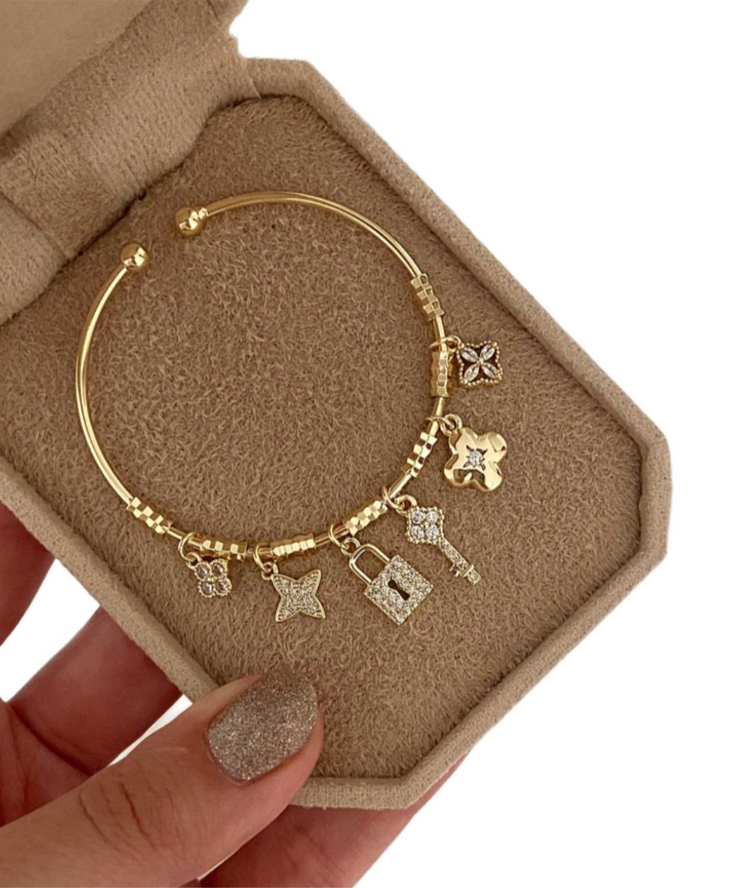 Gold lock and key bracelet with charms on a display card held by a hand.