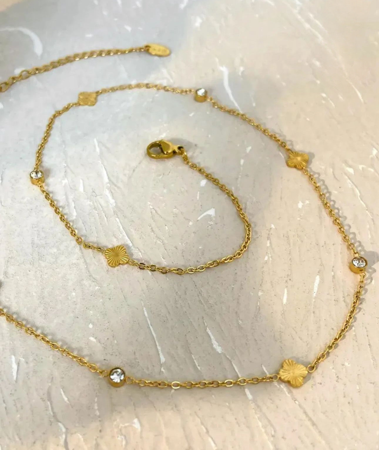 Gold roma clover chain with star and gemstone details on a textured white background