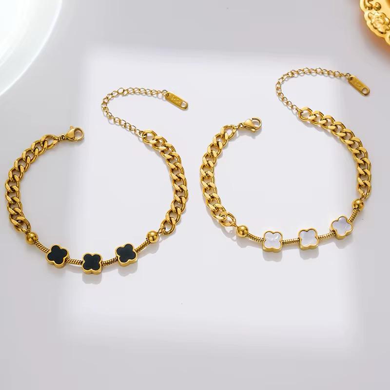 Two gold-colored clover leaf aleena clover bracelets on a white surface, one with black clover leaves and the other with white.