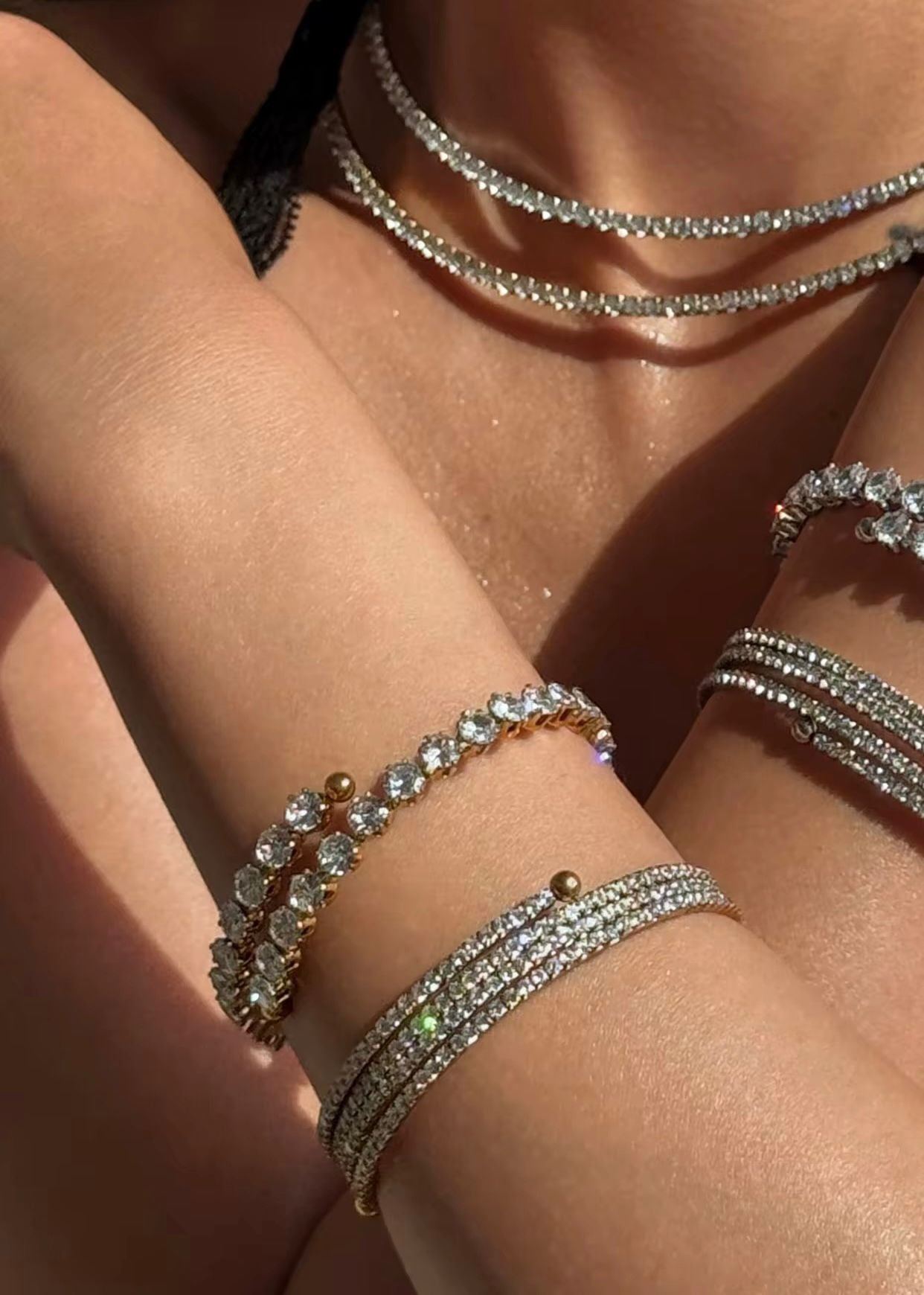 Close-up of a hand wearing multiple diamond-encrusted amiri zircon bracelets on a sunlit skin background