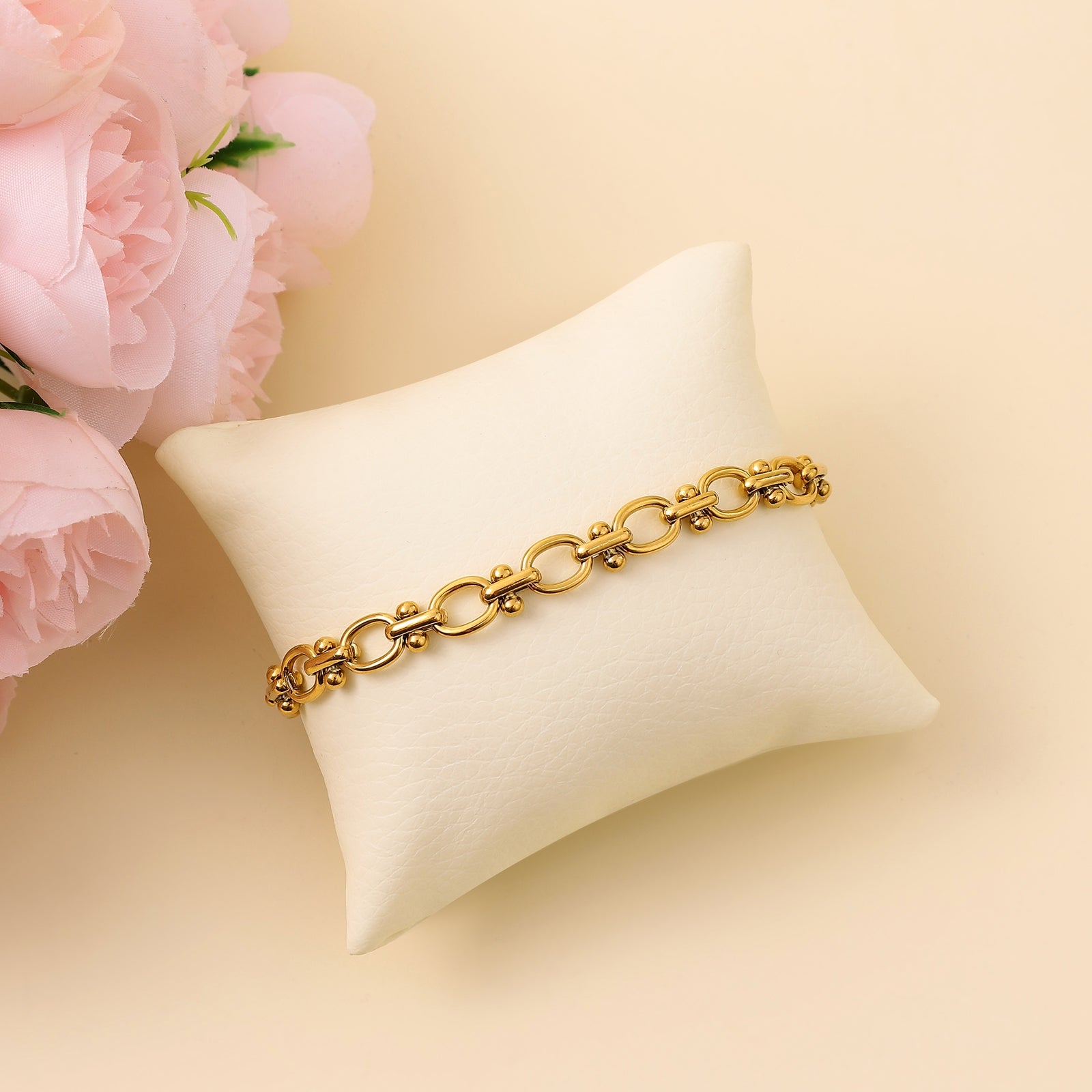 An 18k gold plated block chain bracelet displayed on a white cushion, with a person partially visible in the background.