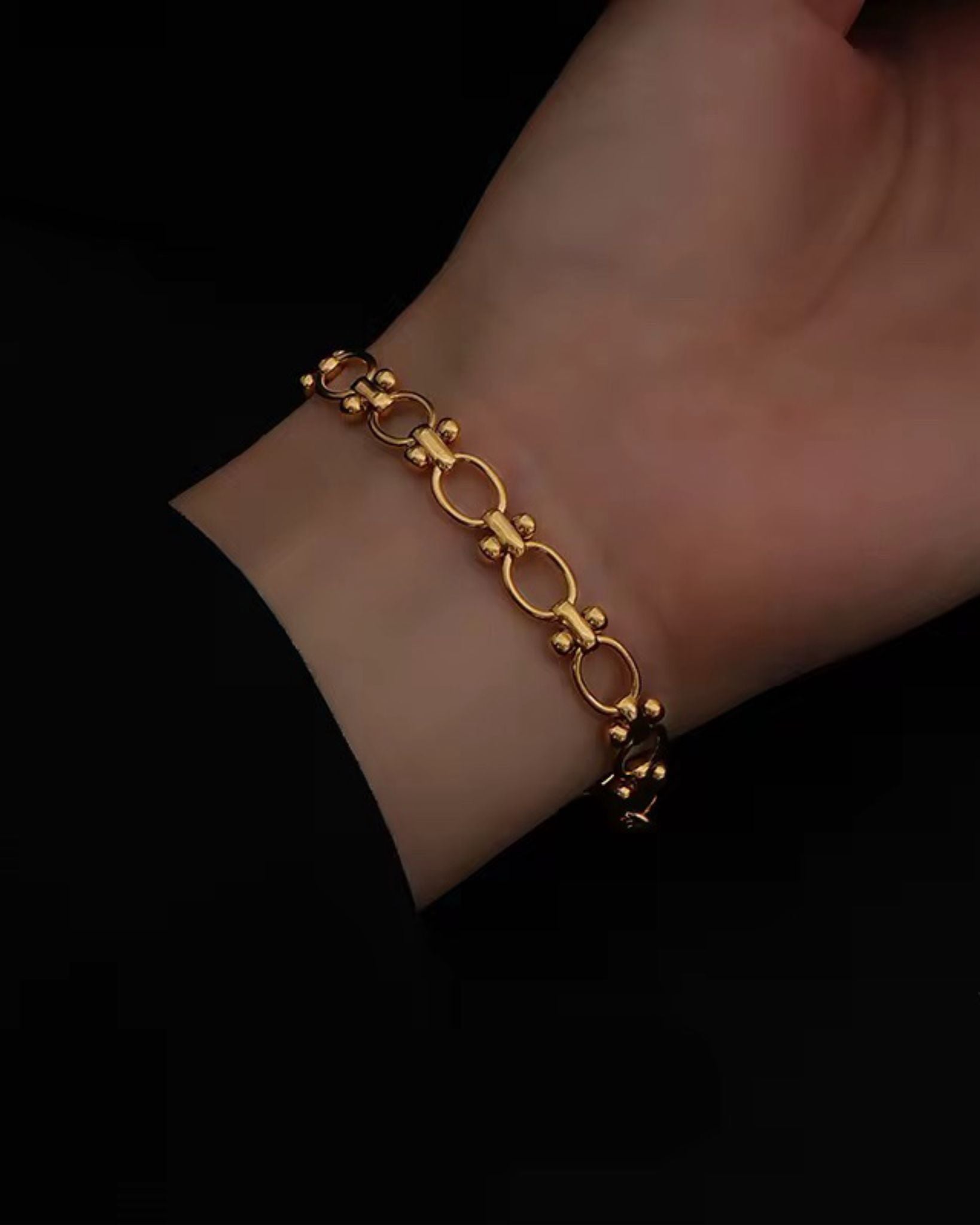 Gold block chain bracelet on a wrist against a black background