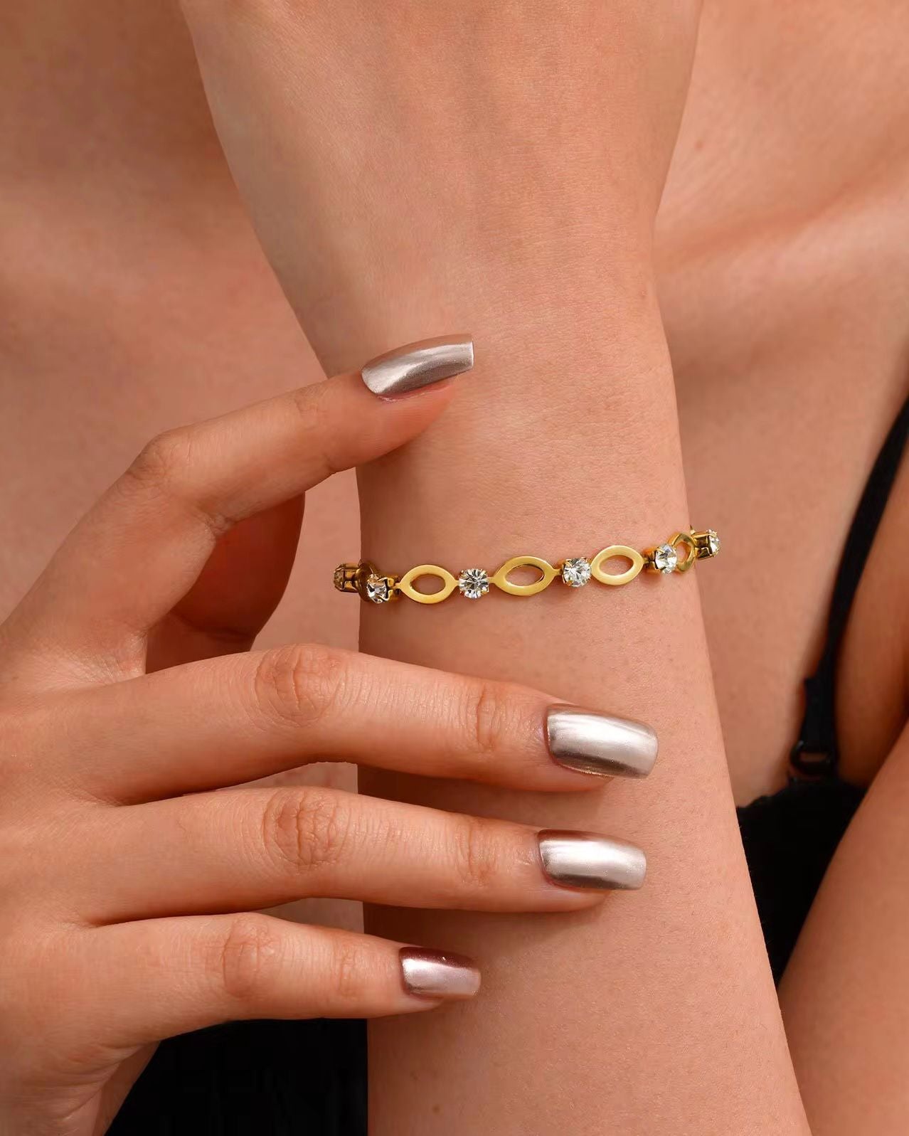 Gold bracelet with infinity symbols on a wrist against a neutral background