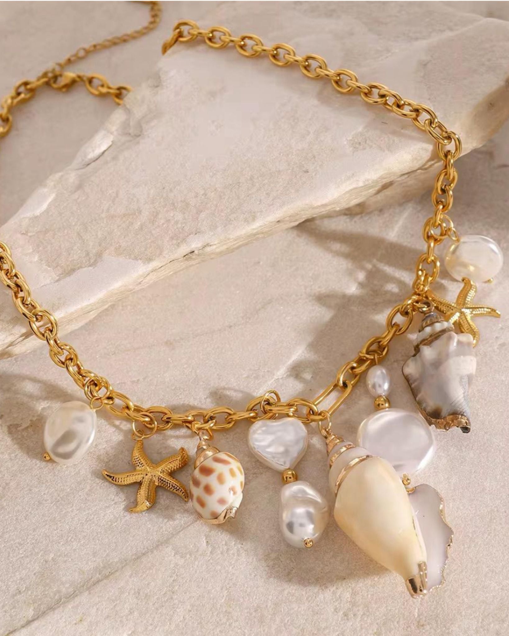Gold bracelet with shell and starfish charms on a stone surface