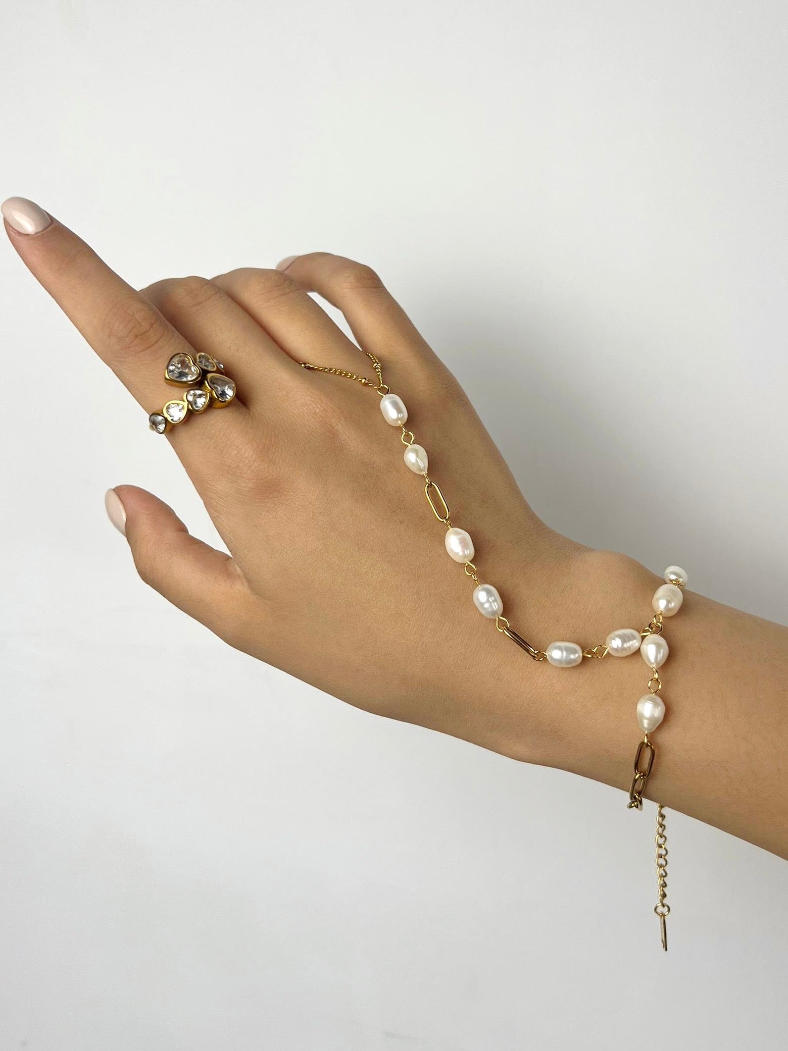 Hand wearing a coast pearl bracelet on a plain background