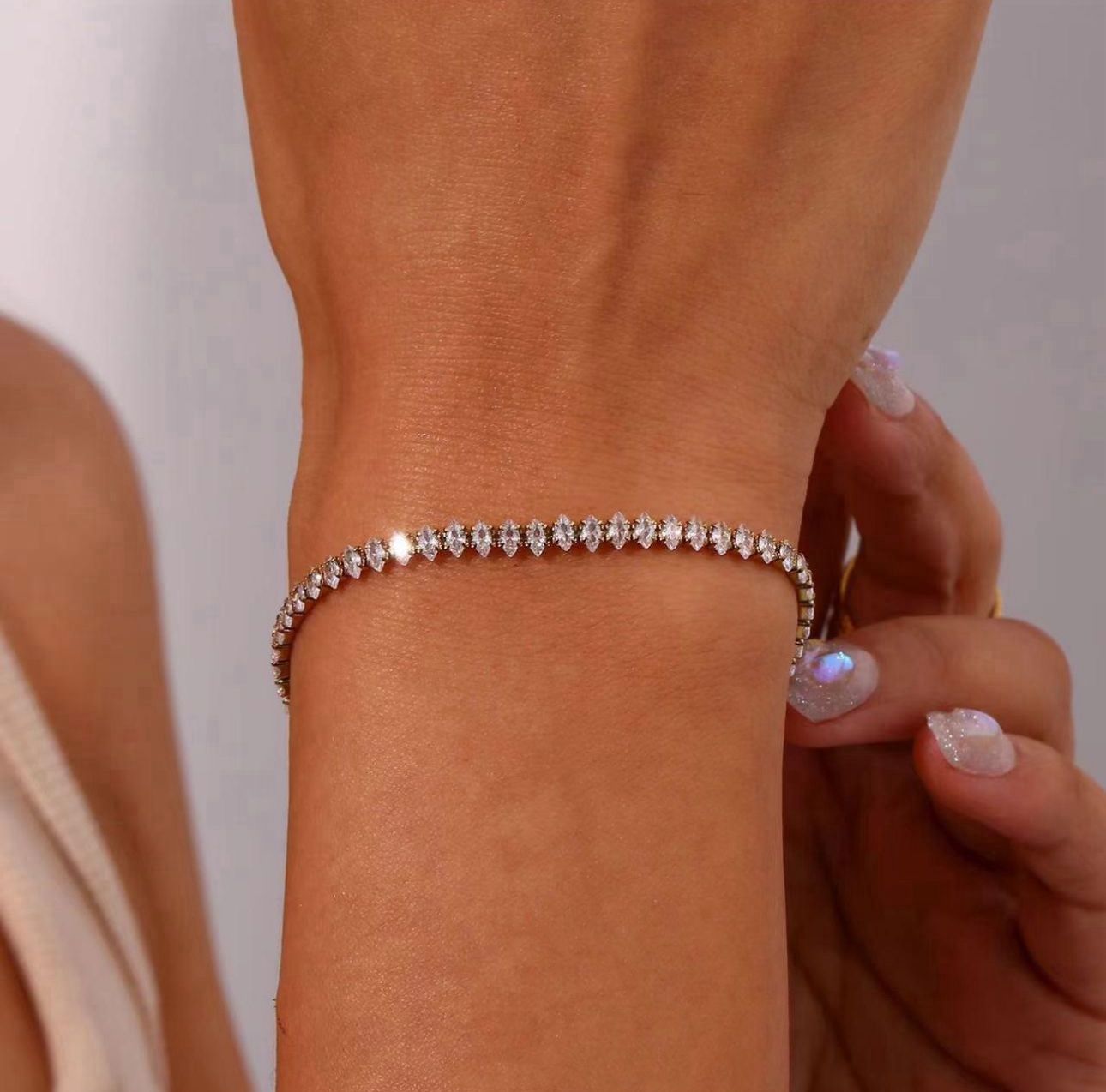 Close-up of a wrist wearing a diamond bracelet against a neutral background