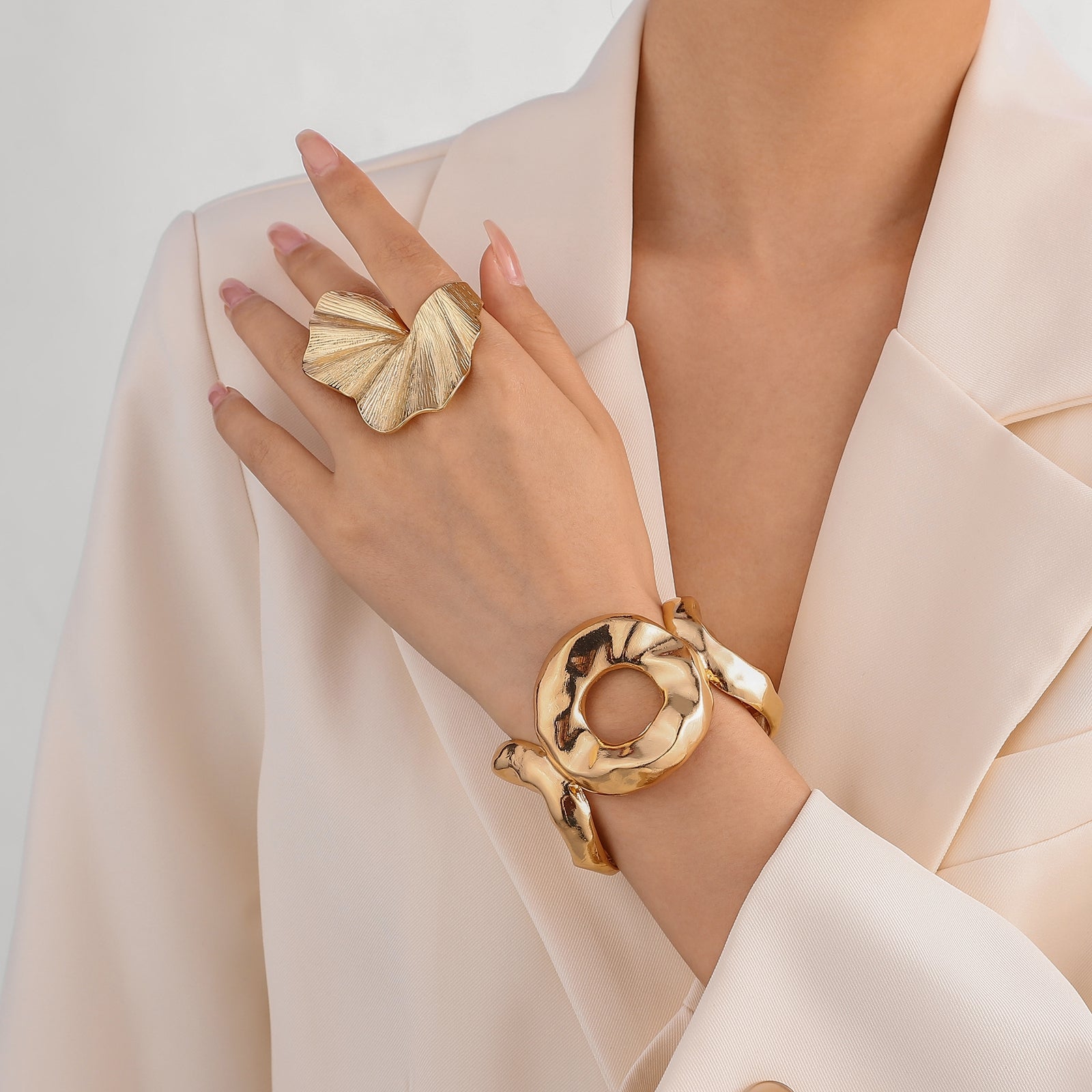 Gold edith ring and bracelet on a hand against a neutral background