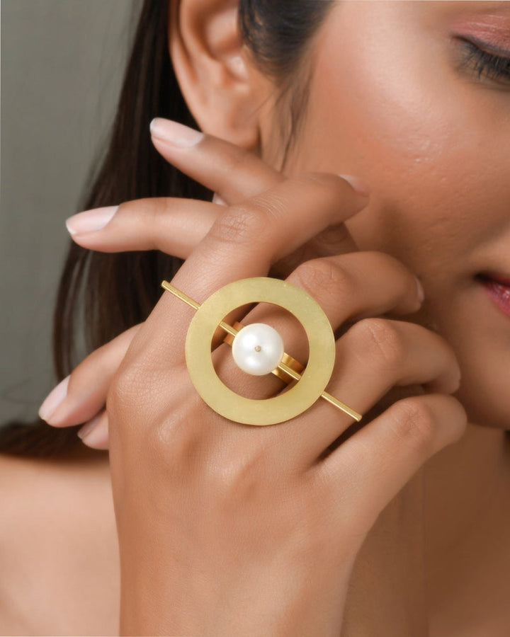 Gold ferra pearl ring with a pearl on a hand against a neutral background