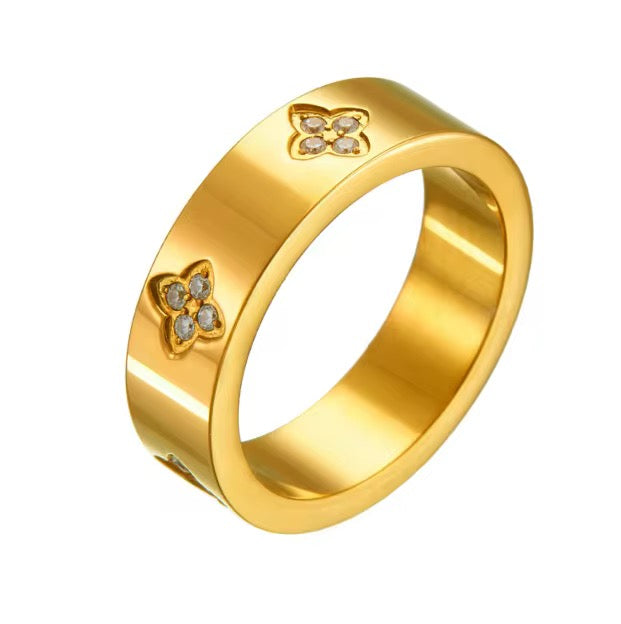 A gold-colored lara clover ring with clover leaf patterns and small inset stones, placed on a white background.