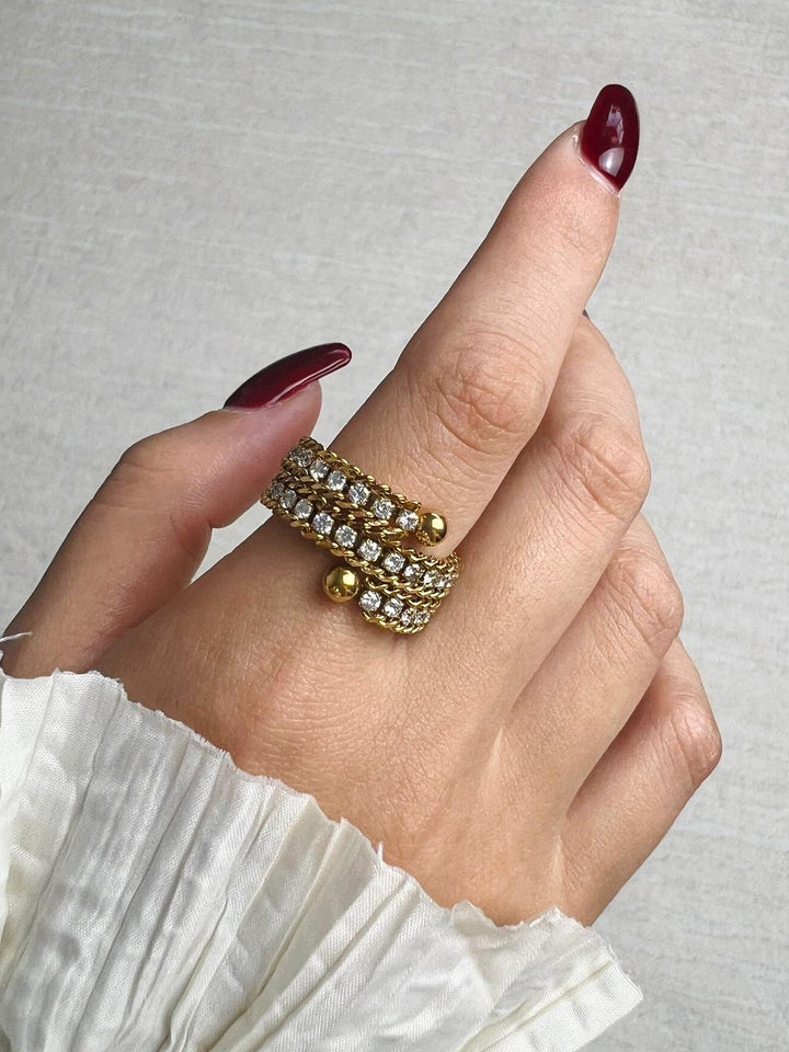 Hand wearing a gold rhinestone ring with a gray background