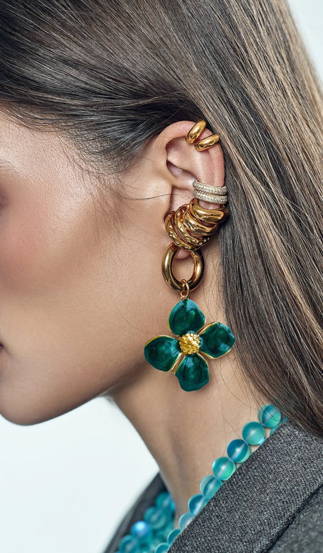Close-up of a person wearing gold earrings and rings with a green floral earring.