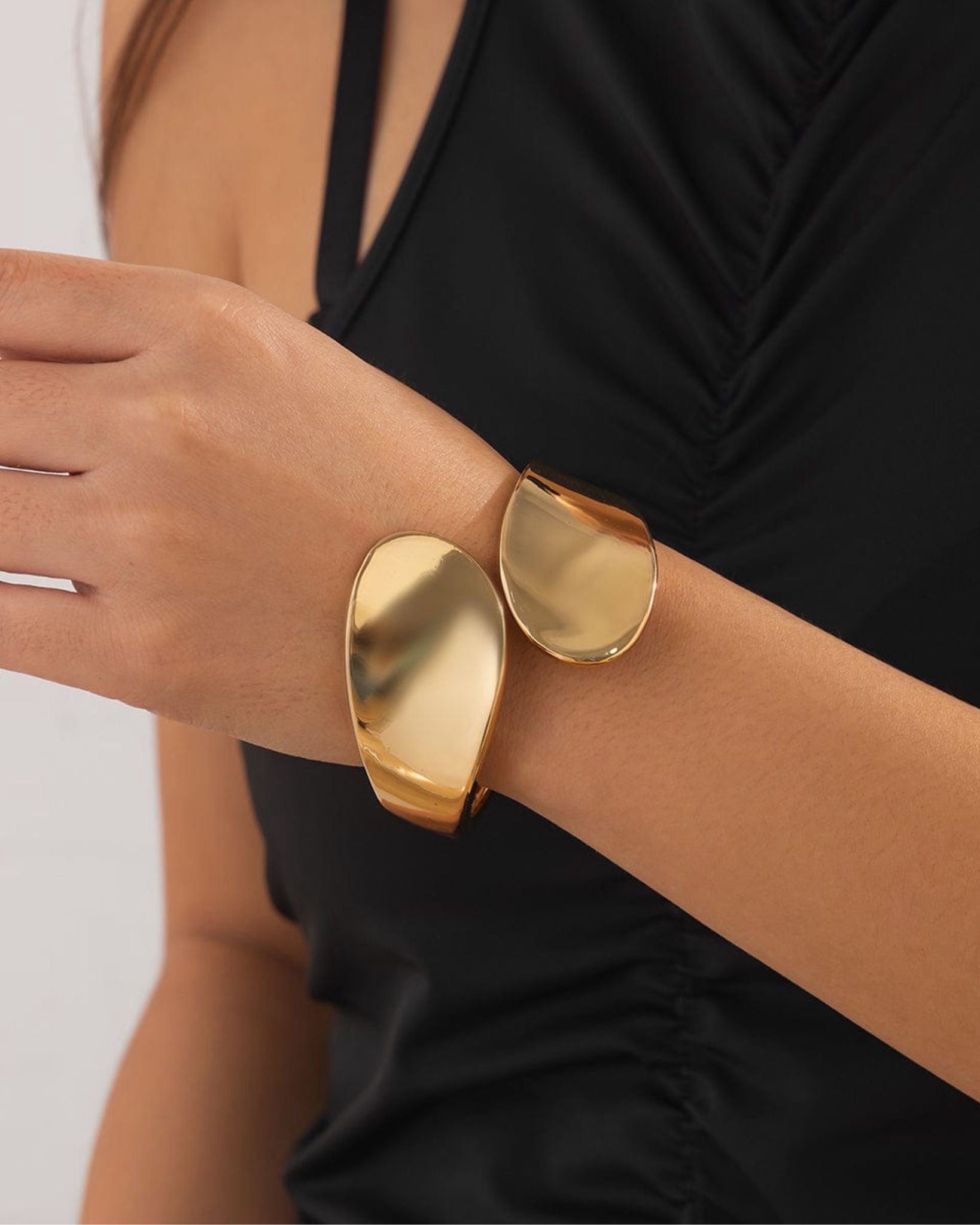Gold cuff ignis bangle on a wrist with a black top and white background