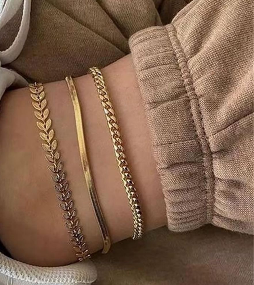 Close-up of a person's wrist wearing multiple gold bracelets on a neutral background