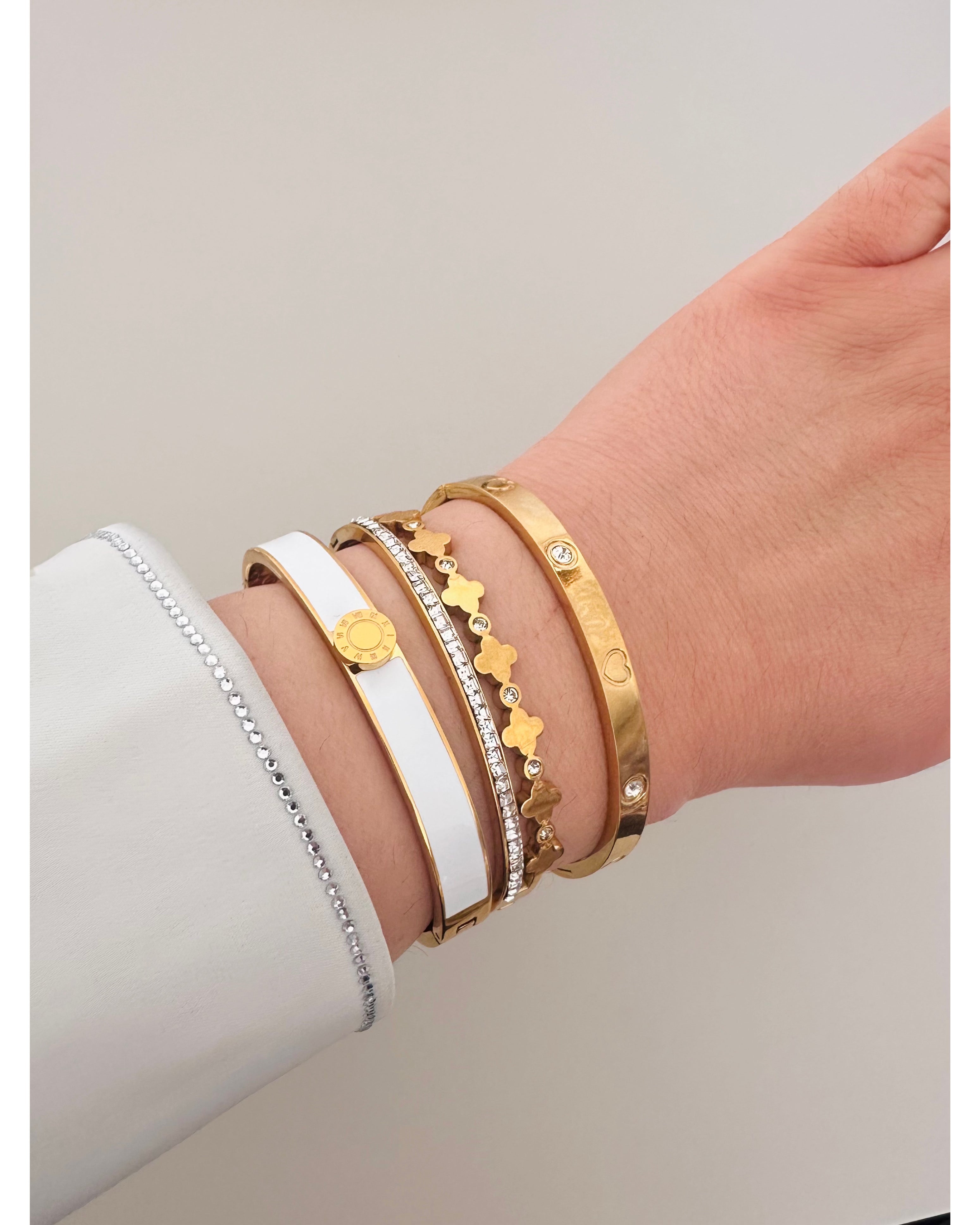 Hand wearing multiple gold bracelets on a light background
