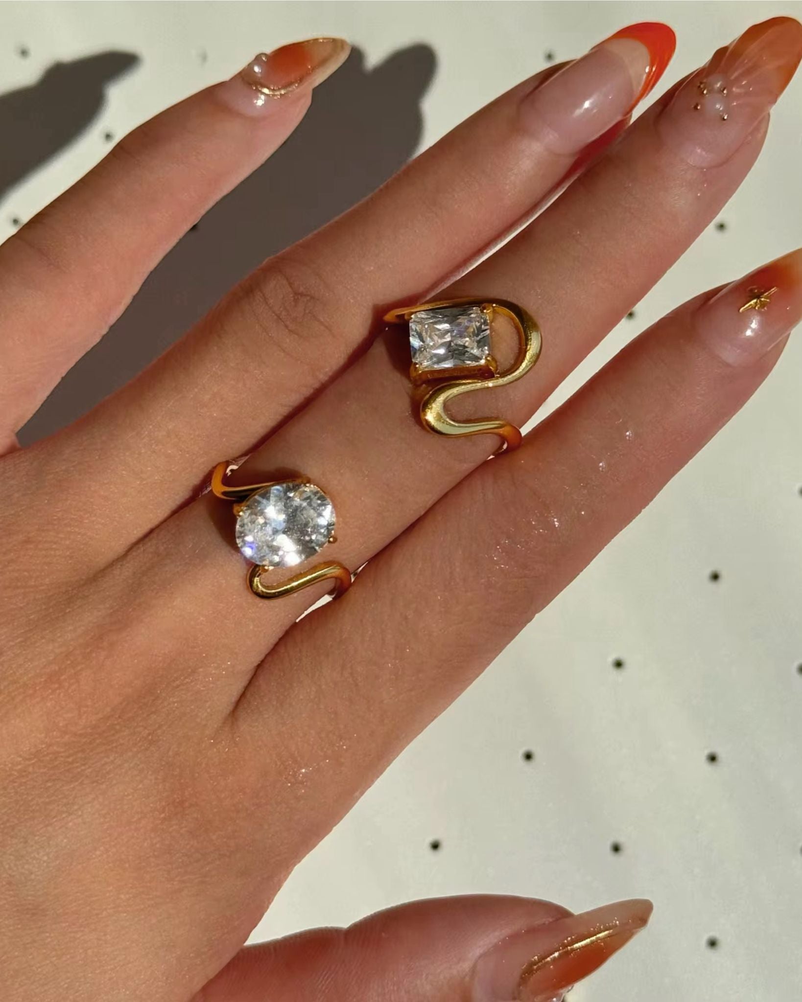 Hand wearing two gold rings with clear gemstones on a light background