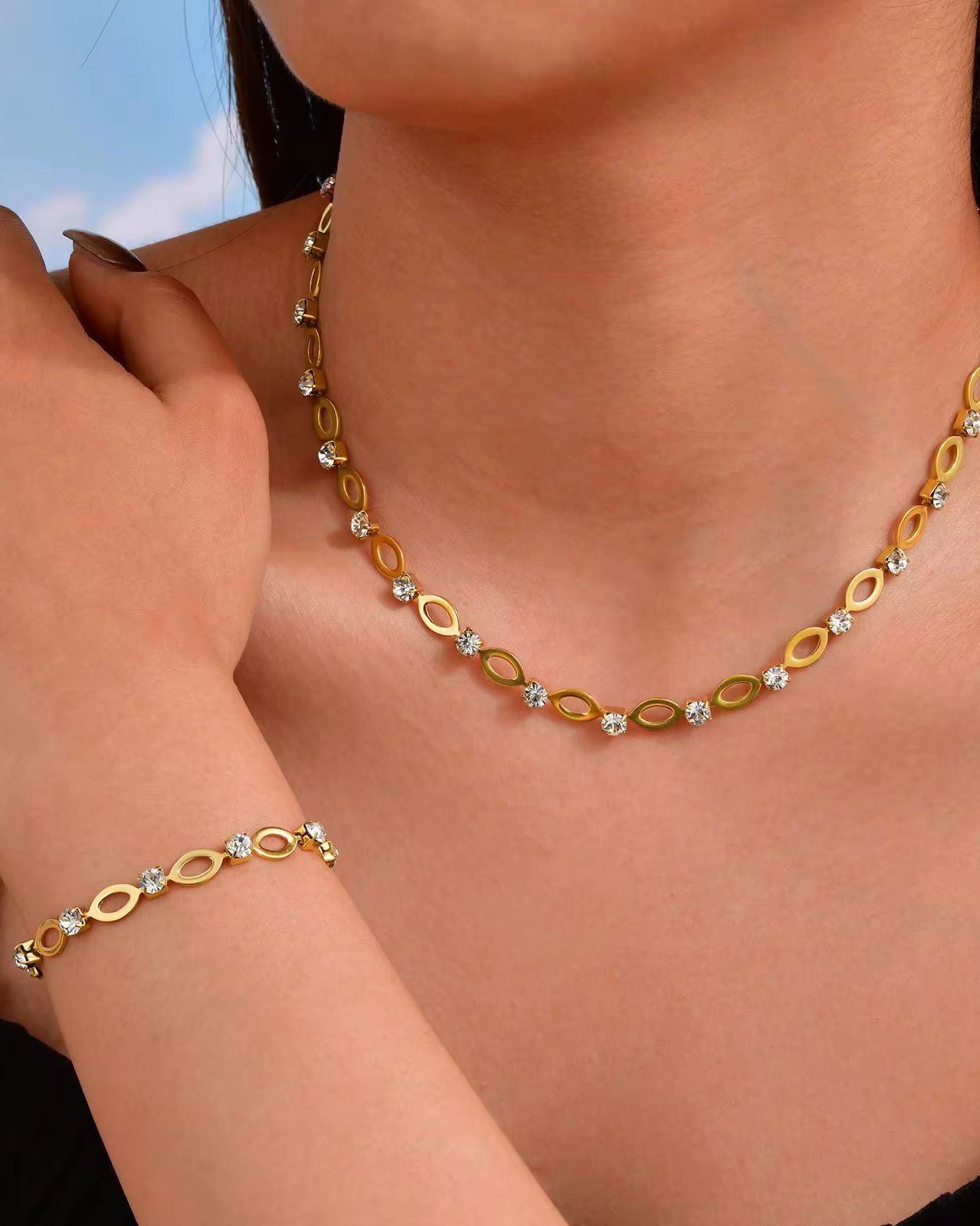 Gold necklace with small diamonds on a person's neck and arm against a neutral background