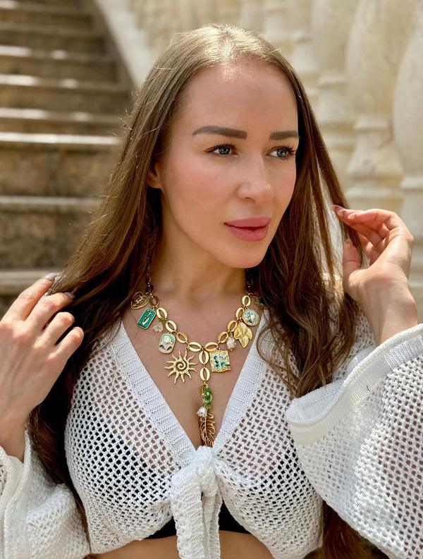 Woman wearing a white top and gold necklace with green gemstones outdoors.