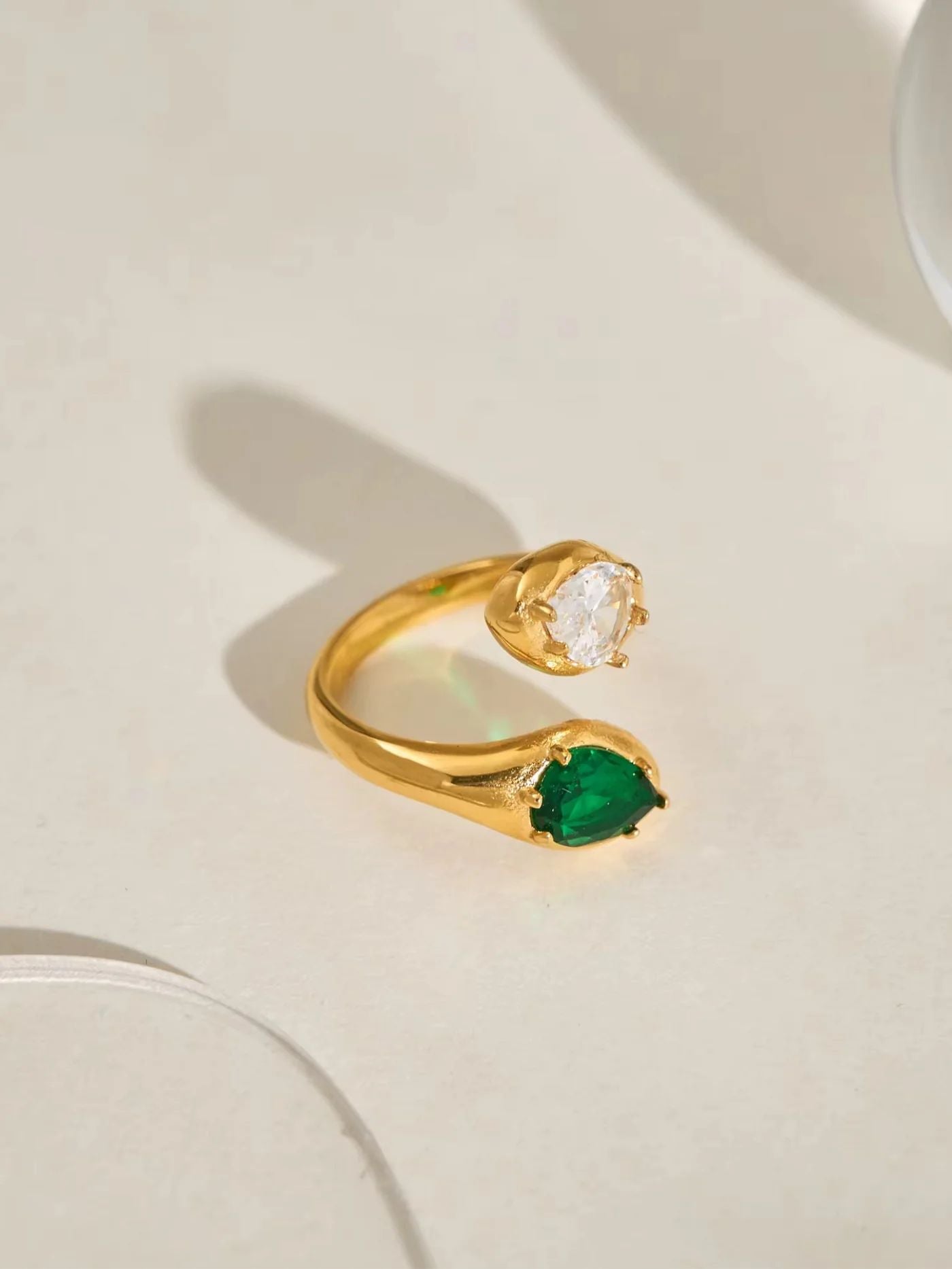 Gold patricia ring with green gemstone on a light beige background