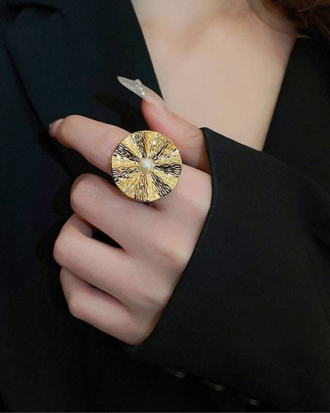 Gold pearl orbit ring with a central gemstone held by a person wearing a black outfit.