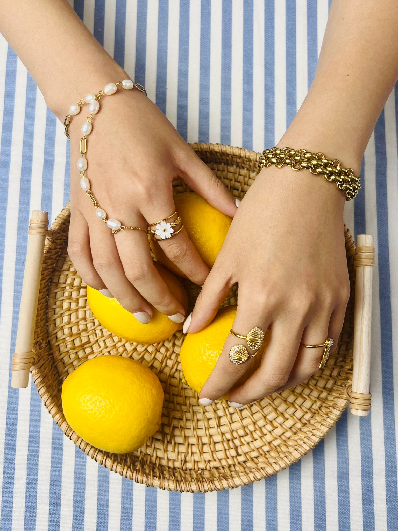 Hands with jewellery holding lemons on a woven tray against a striped background