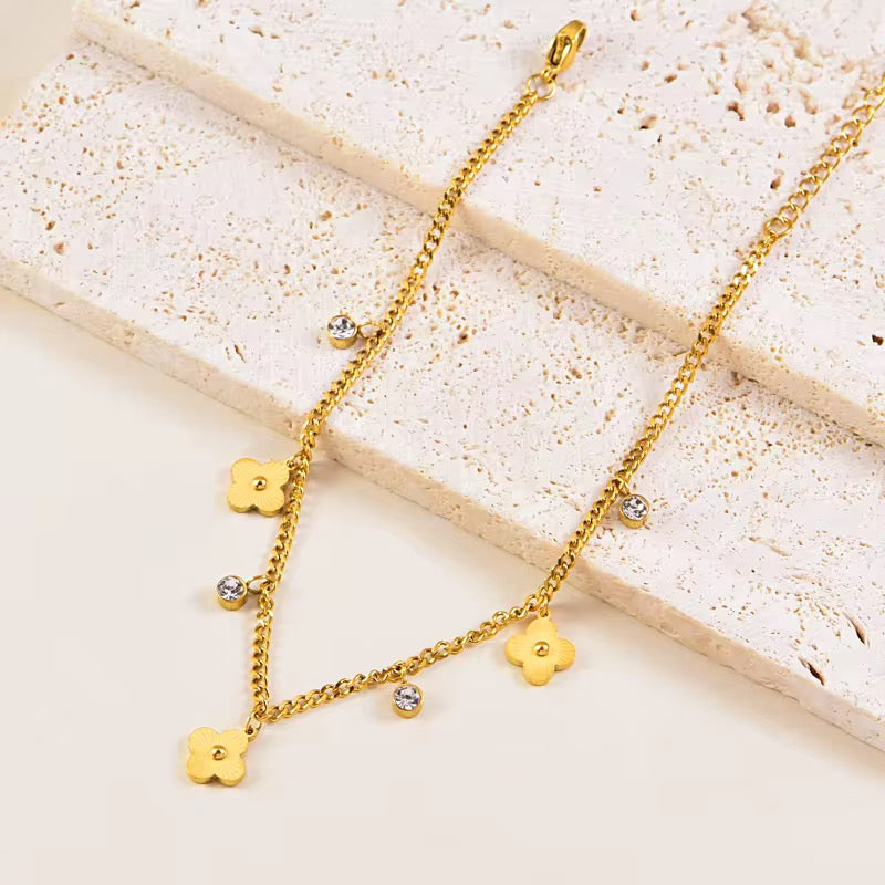 Gold necklace with roma clover-shaped chain and pendants on a textured surface