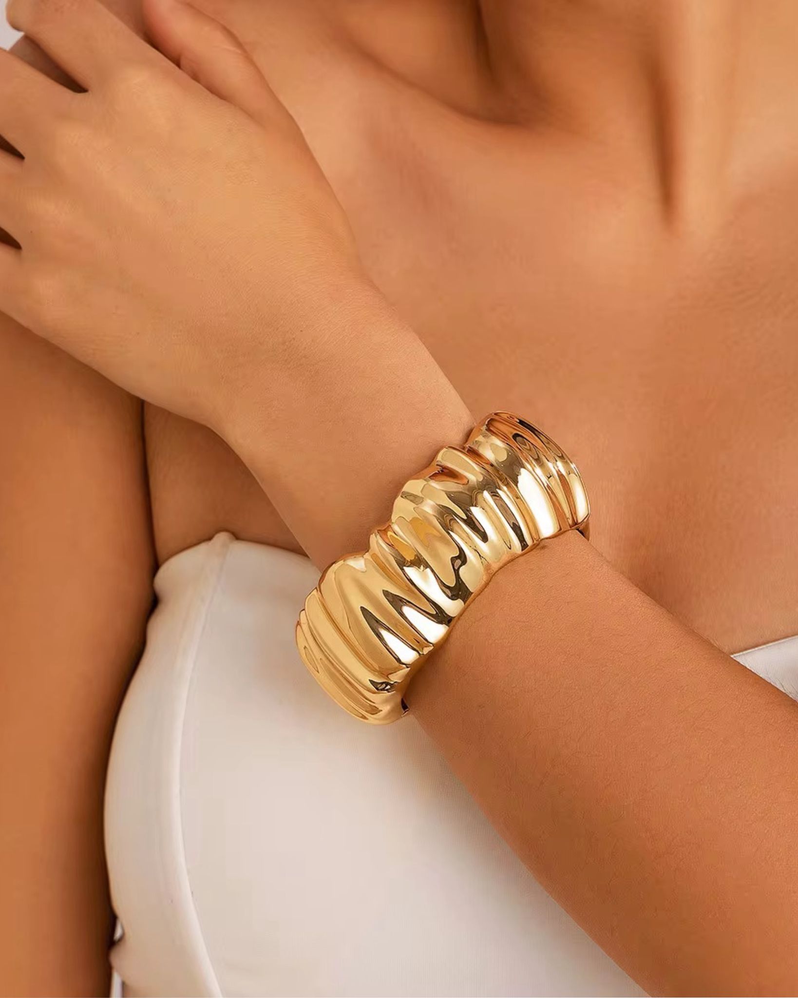 Gold rumi bangle on a wrist with a neutral background