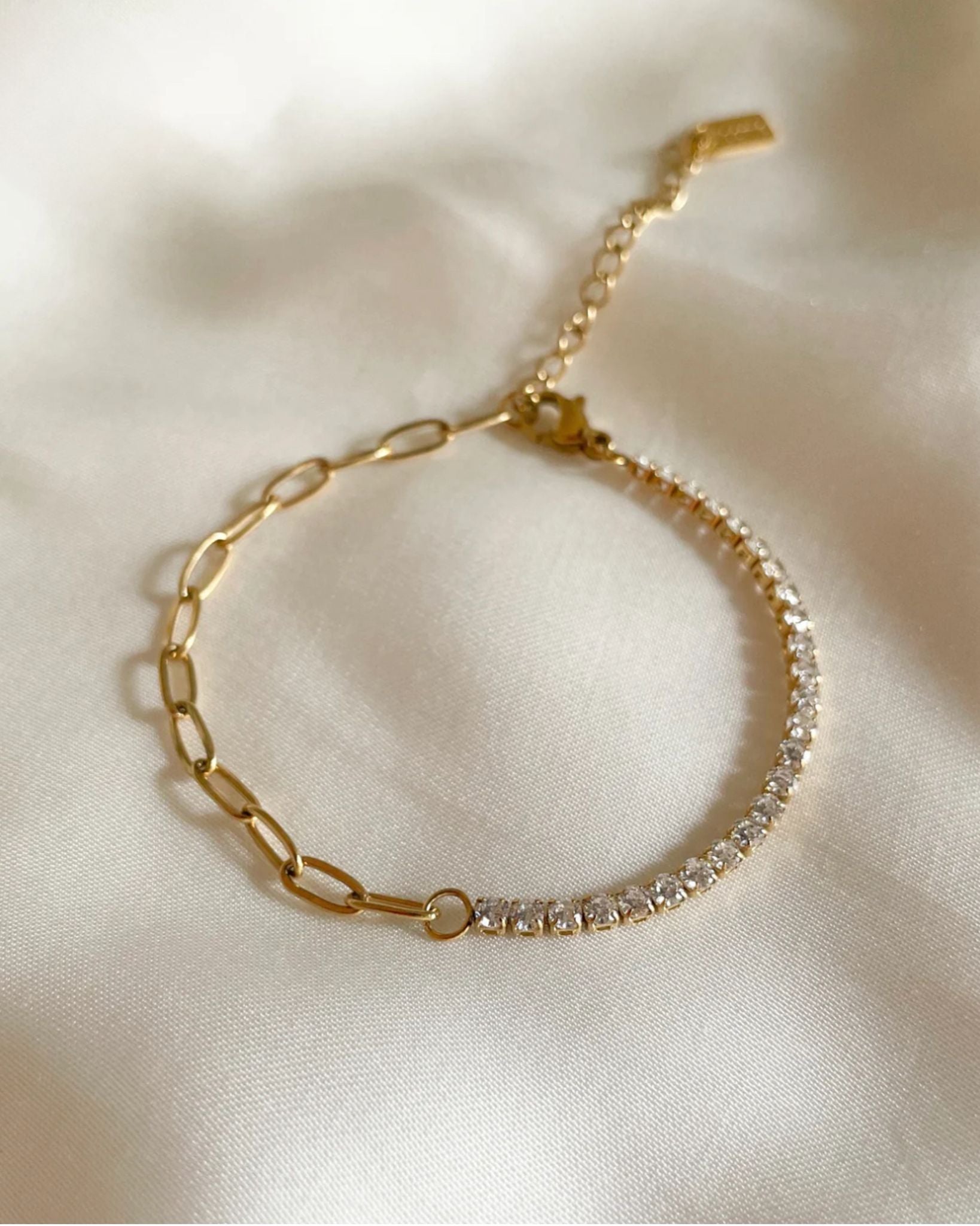 Gold tennis paper-clip bracelet with diamond accents on a light fabric background