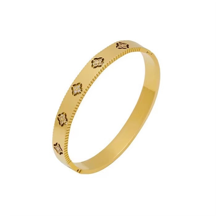 A gold-colored theodora clover bangle with clover patterns, made of stainless steel with cubic zirconia accents.