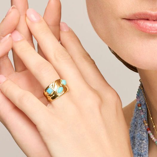Gold ring with turquoise stones on a hand against a neutral background