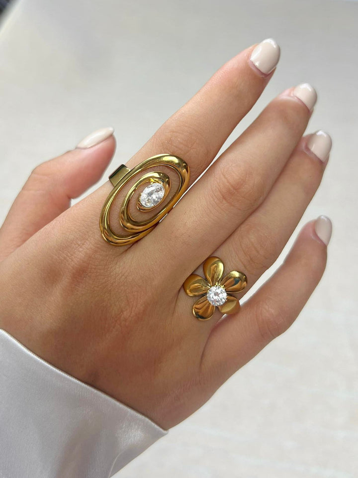 Hand wearing two gold rings with clear gemstones on a neutral background