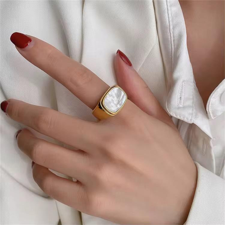 Hand wearing a gold white shell ring with a white stone against a white background
