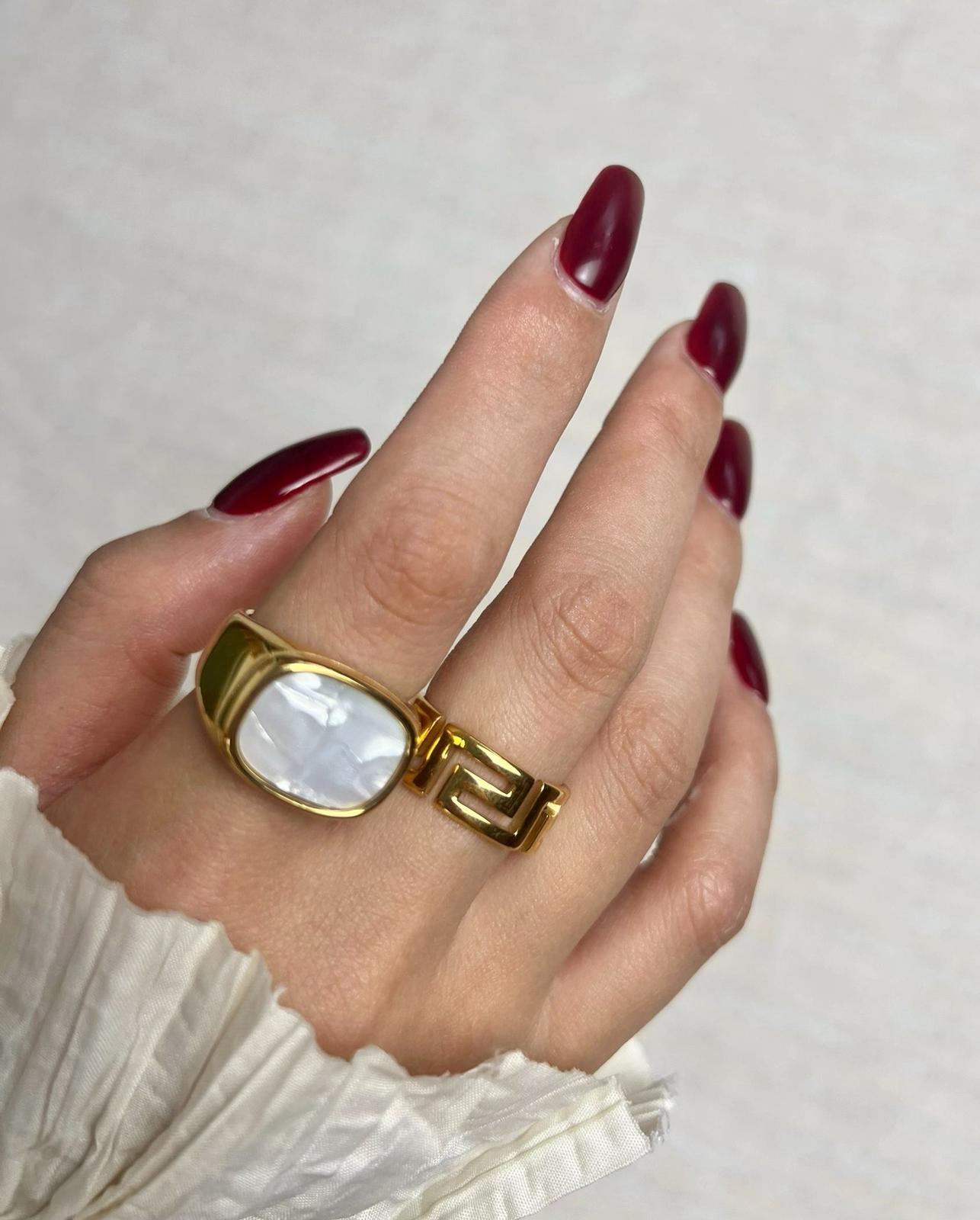 Gold white shell & ariande ring on a finger with red nail polish against a neutral background